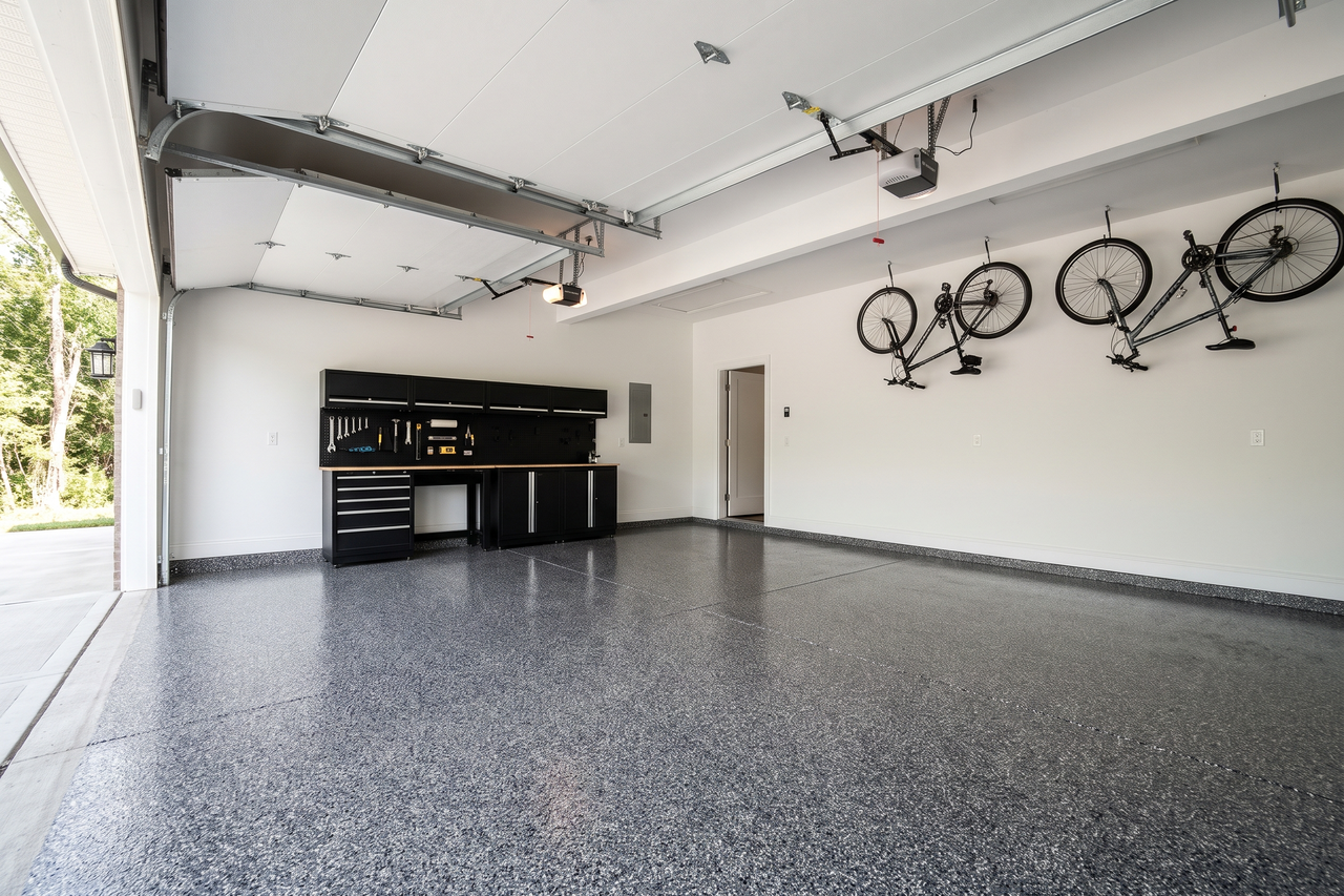 Attached two-car garage with a charcoal and white flake coated floor, a black workbench along the side wall and two bicycles hanging from ceiling hooks