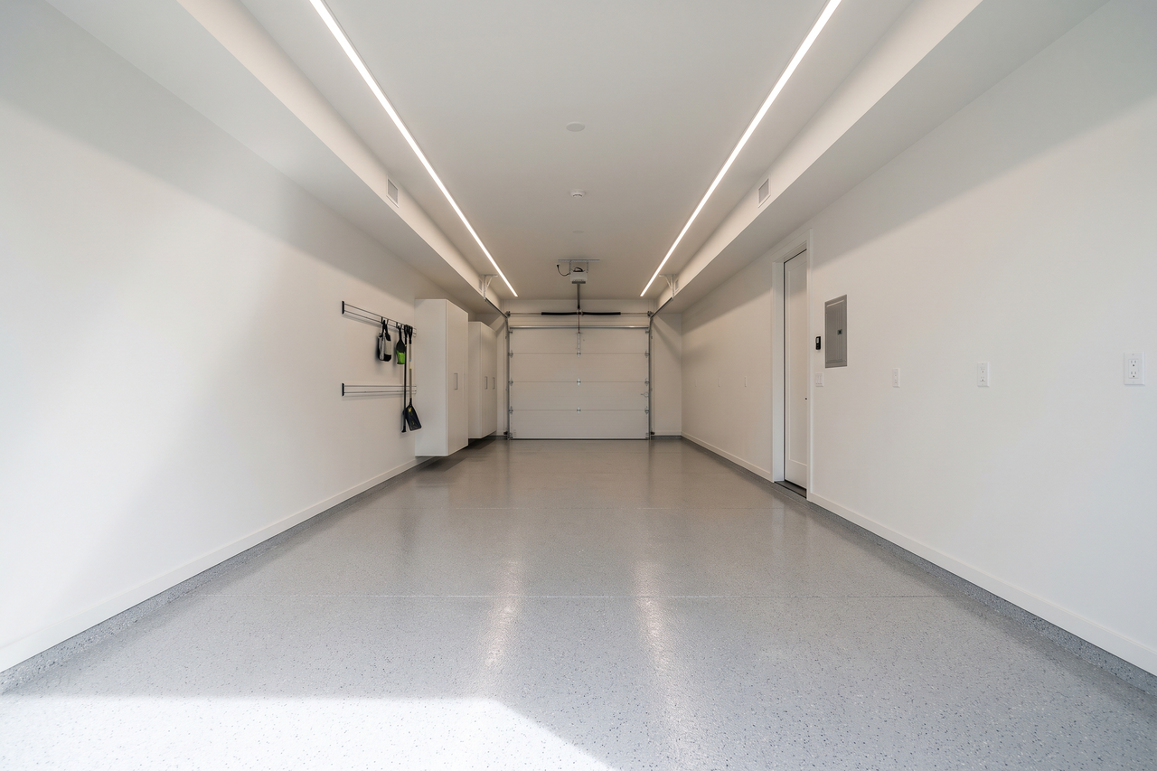 Long tandem garage with a smooth light gray flake floor reflecting soft overhead light and a closed white overhead door at the far end